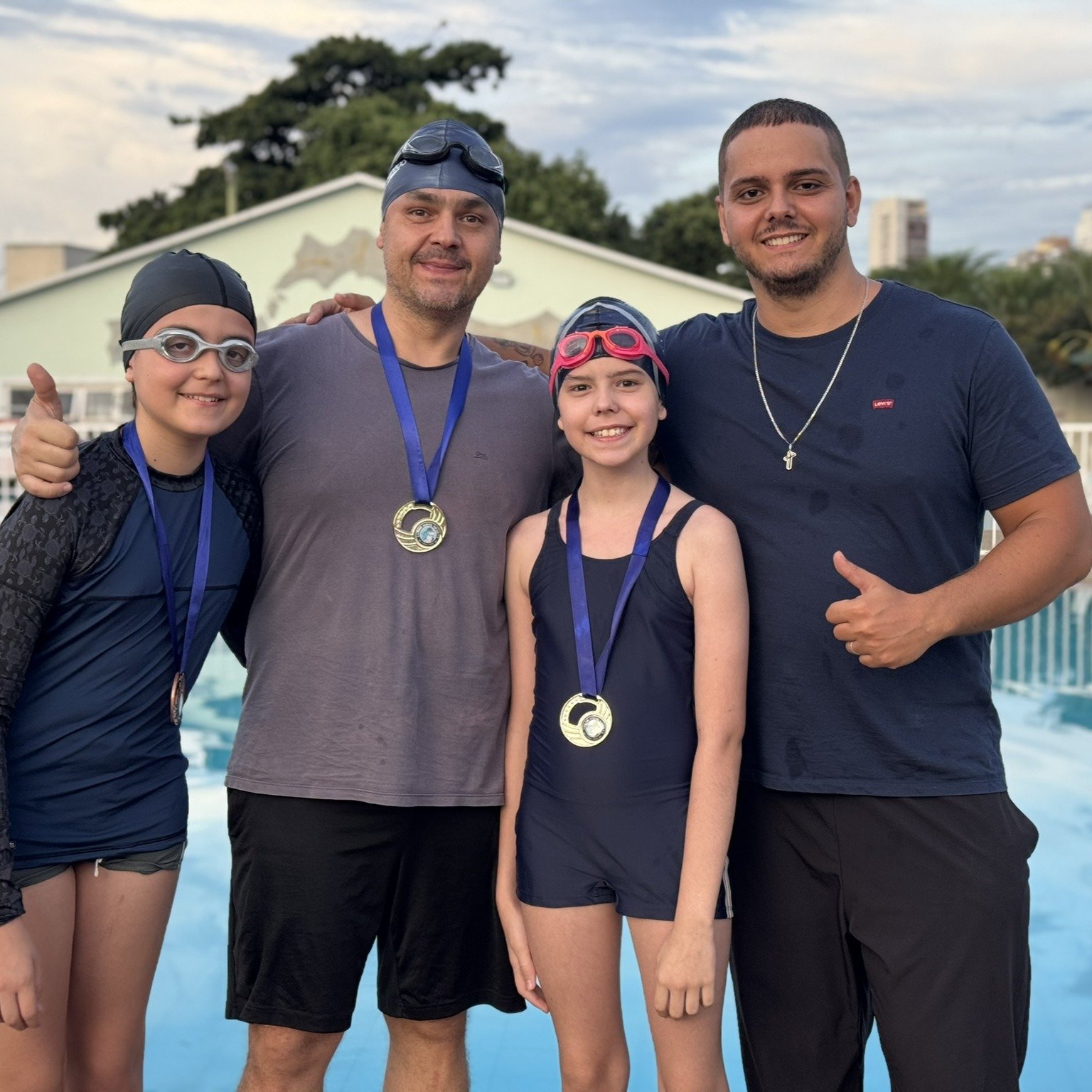 3 alunos de natação fazendo pose para a foto juntos ao professor Filipe, mostrando as medalhas que ganharam no rankeamento interno da natação