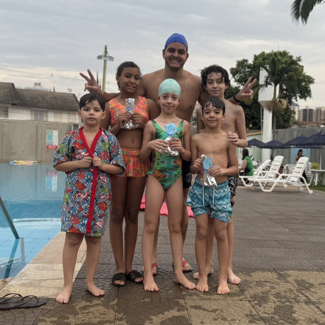 5 alunos de natação fazendo pose para a foto juntos ao professor Filipe, mostrando a lembrancinha que ganharam no dia das crianças
