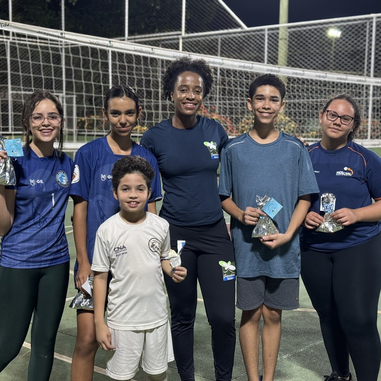 5 alunos de vôlei fazendo pose para a foto juntos a professora Thais, mostrando a lembrancinha que ganharam no dia das crianças